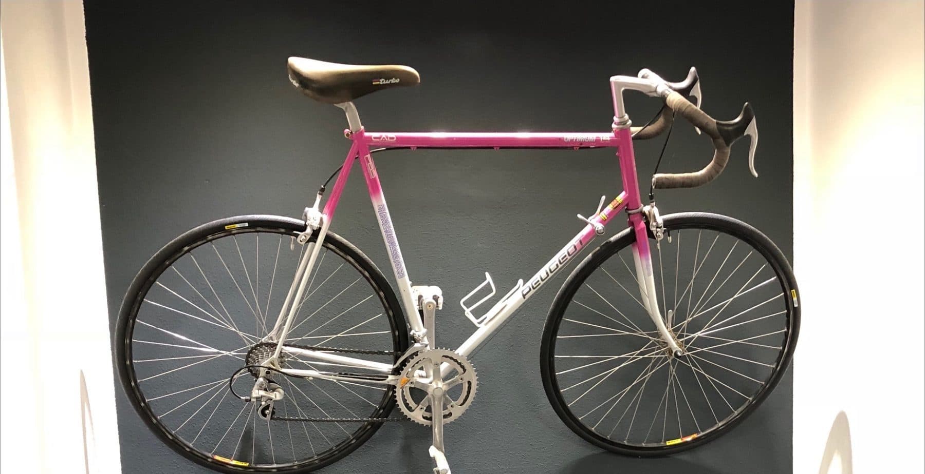 Peugeot-Rennrad in Pink und Weiß an dunkler Wand
